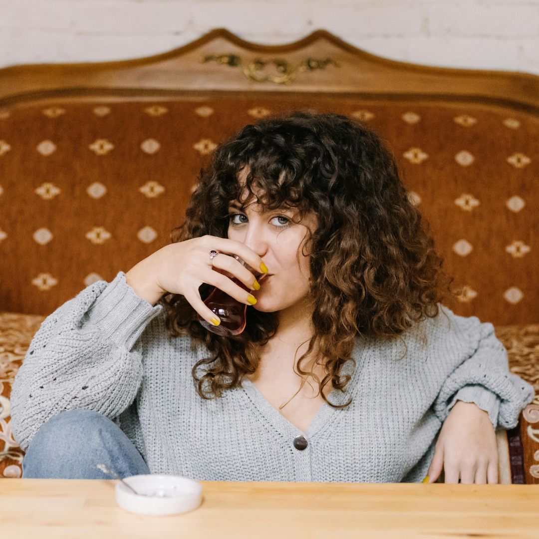 A woman relaxing on a vintage sofa sipping Turkish tea from a tulip glass while watching a Turkish drama